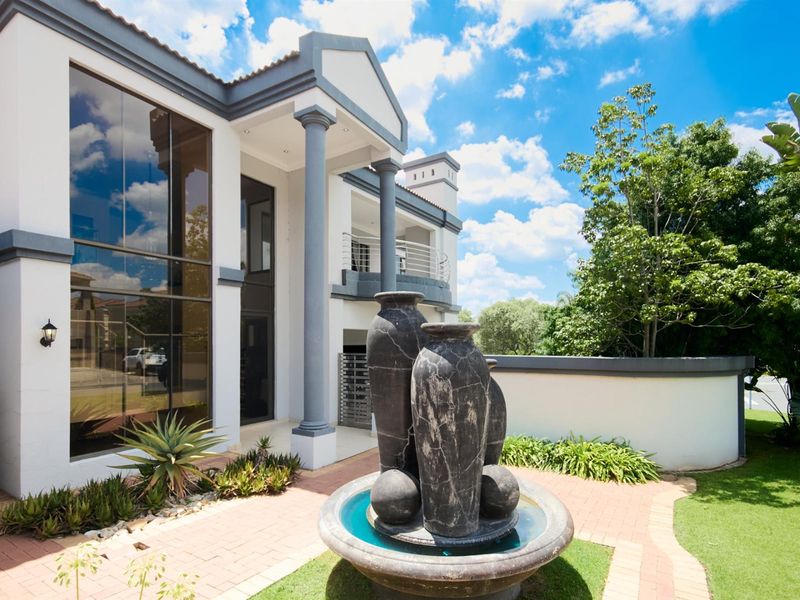 A well-maintained exterior front facade featuring large glass windows, decorative columns, a paved entrance area, and a central water feature in the garden.