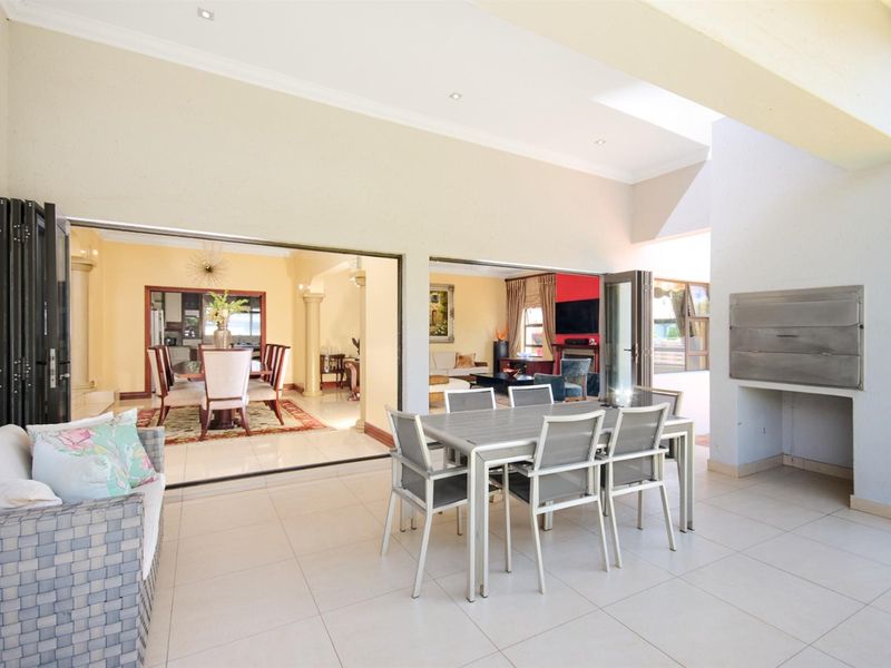 Spacious covered patio featuring built-in braai, tiled flooring, and large folding doors providing seamless indoor-outdoor flow to the open-plan living and dining areas.