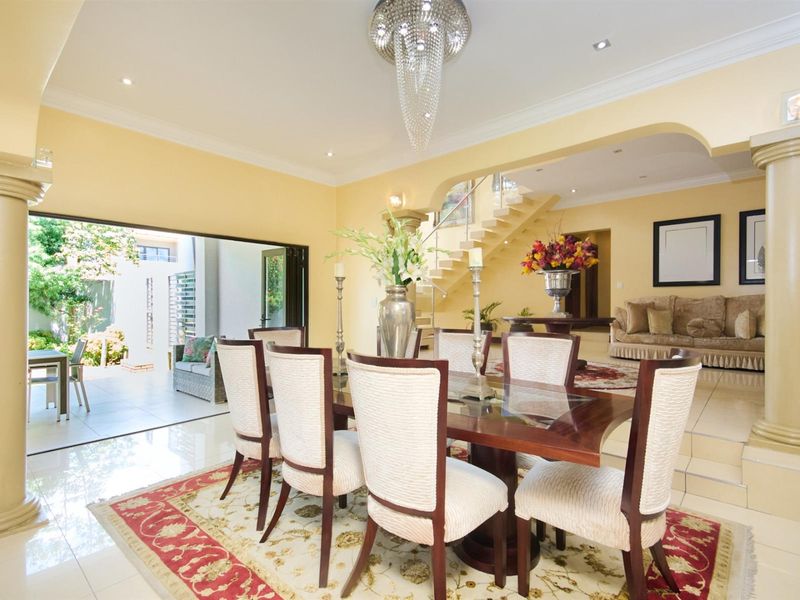 Spacious open-plan dining and living area featuring polished tile flooring, decorative columns, a grand staircase, and seamless access to an outdoor patio.