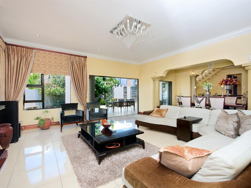 Spacious open-plan living area featuring polished tile flooring, decorative ceiling coving, a modern chandelier, and large sliding doors leading to an outdoor patio.