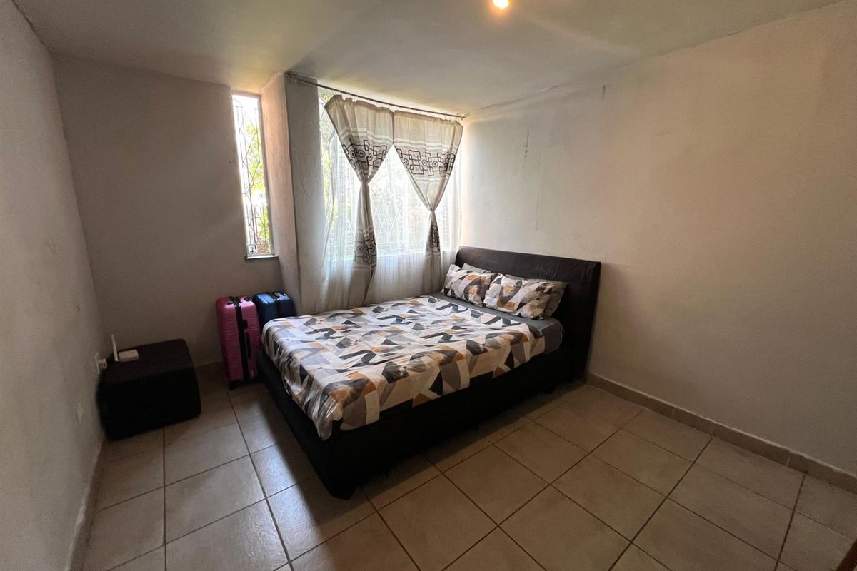 A bedroom featuring tiled flooring and a window with security bars, requiring cosmetic updates to the wall finishes.