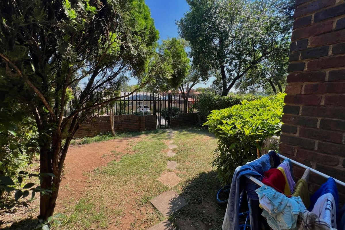 A private rear garden area featuring a lawn, stone pathway, and secure metal gate access, enclosed by a brick boundary wall.