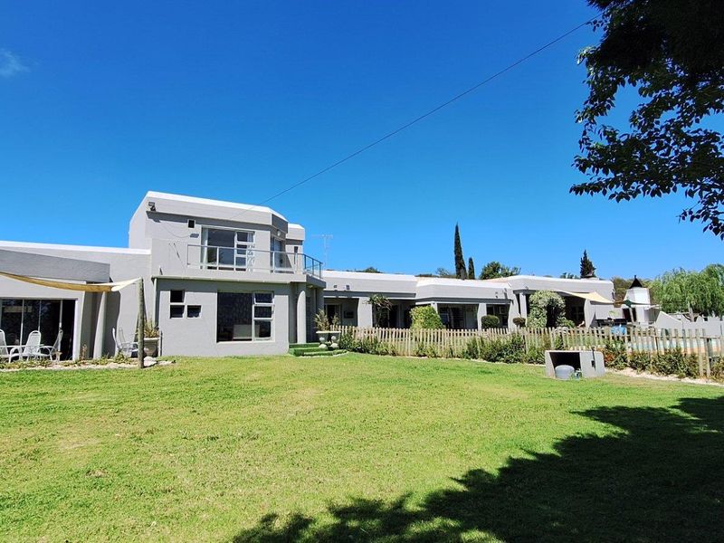 Spacious rear exterior view of the farm property featuring a large manicured lawn, multi-level building structure, and integrated balcony area.