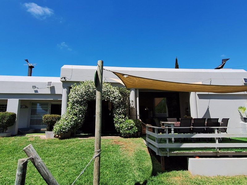 Rear view of the farm property featuring a covered patio area, raised wooden deck, and well-maintained lawn with established garden landscaping.