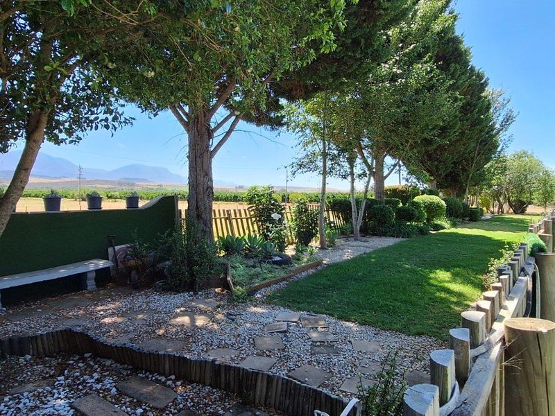 A well-maintained garden area featuring mature trees, a gravel pathway, lawn, and a wooden fence, offering scenic views of the surrounding landscape.