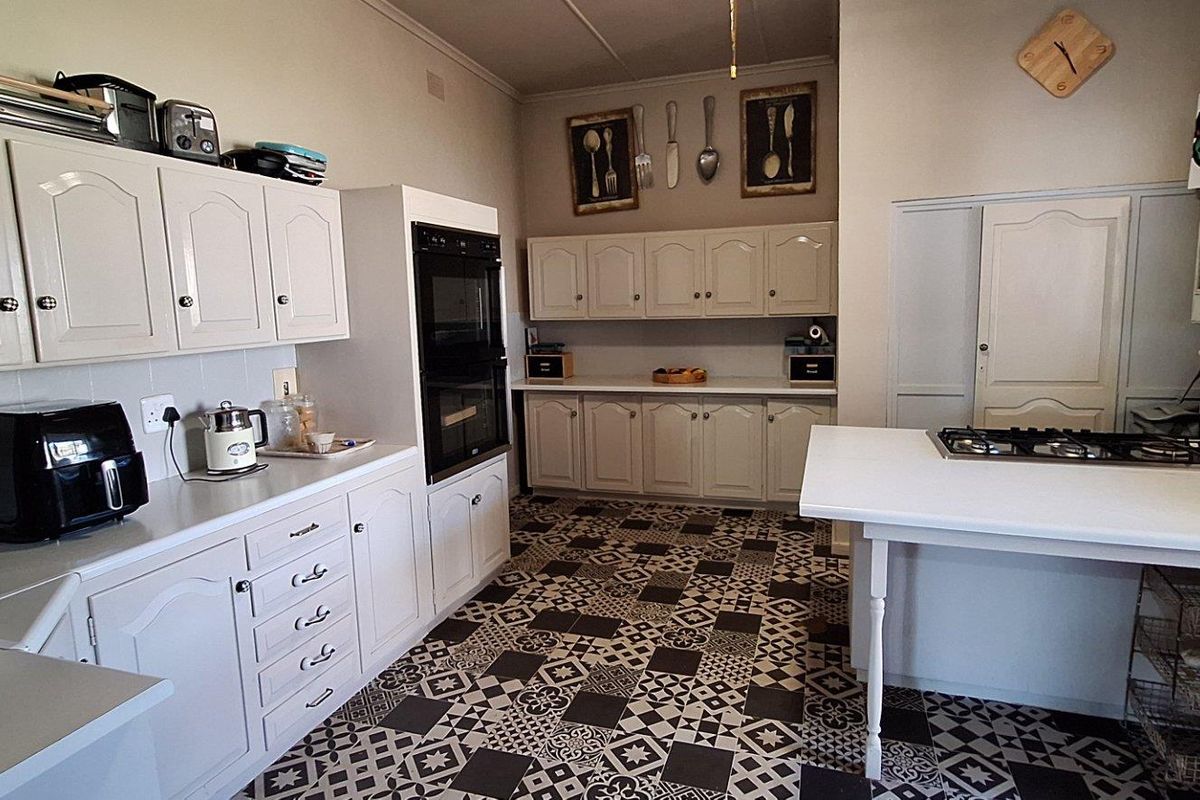 A functional kitchen featuring white cabinetry, a built-in oven, a central island with a gas hob, and patterned tile flooring.