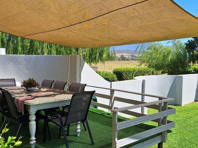 A covered outdoor patio area featuring a built-in brick fireplace, artificial turf flooring, and views over the surrounding farm landscape.