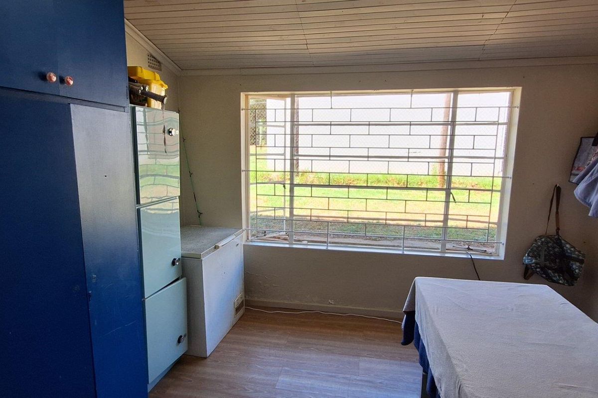A functional utility room or bedroom featuring built-in blue cabinetry, wood-look flooring, and a large window with security bars.