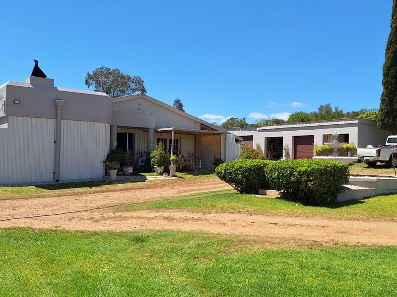 A view of the farm property featuring a main dwelling with attached garage structures, surrounded by established lawns and mature landscaping.