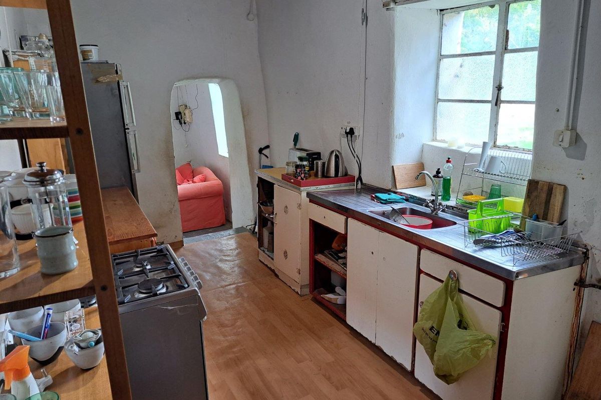 A rustic kitchen featuring a stainless steel sink, built-in cabinetry, and a gas stove, with an arched doorway leading to an adjacent living space.