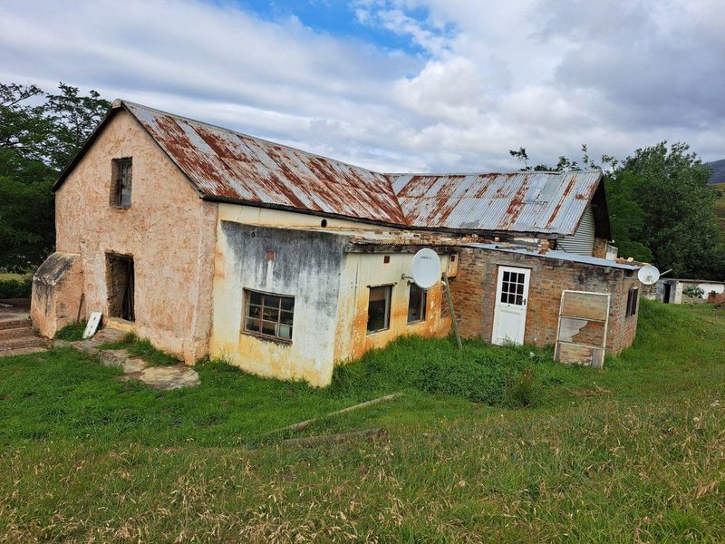 A rustic farmhouse exterior featuring a weathered corrugated metal roof and aged masonry walls, set within a rural landscape.