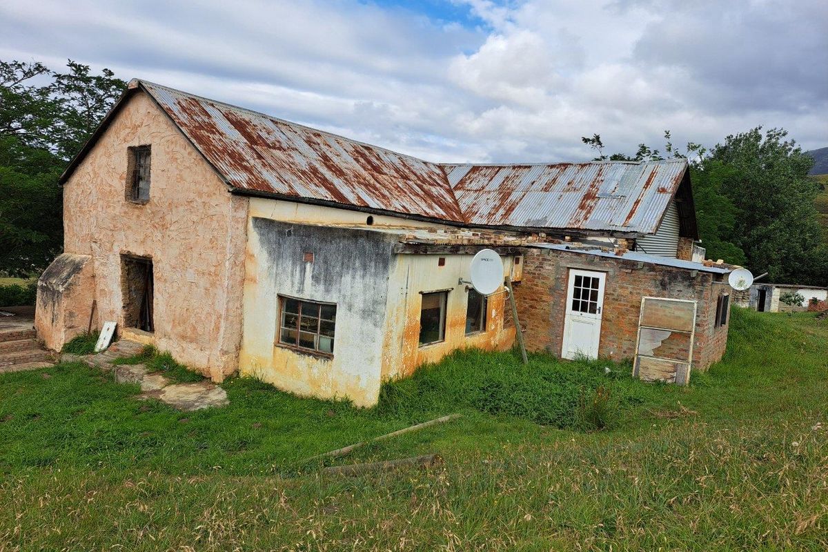 A rustic farmhouse exterior featuring a weathered corrugated metal roof and aged masonry walls, set within a rural landscape.
