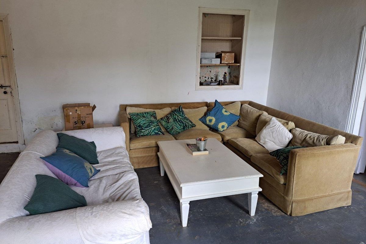 A living room area featuring a built-in wall niche, painted concrete flooring, and plain wall finishes in need of maintenance and refurbishment.
