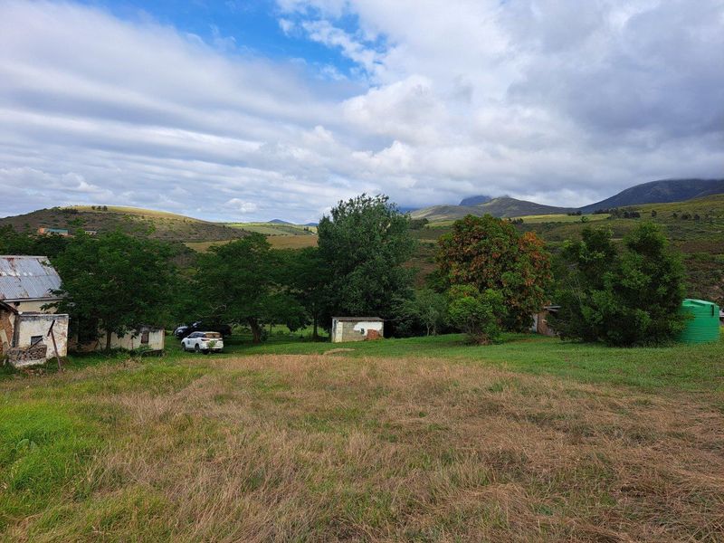 A wide-angle view of a rural farm property featuring outbuildings, a water tank, and expansive mountain landscape views.