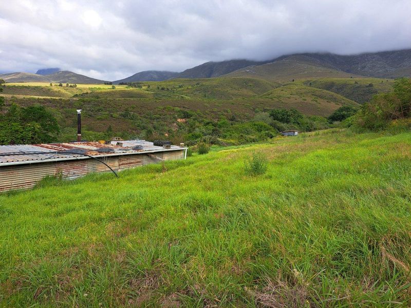 A view of a rural farm property featuring a small, weathered outbuilding with a corrugated metal roof set against a scenic mountain landscape.