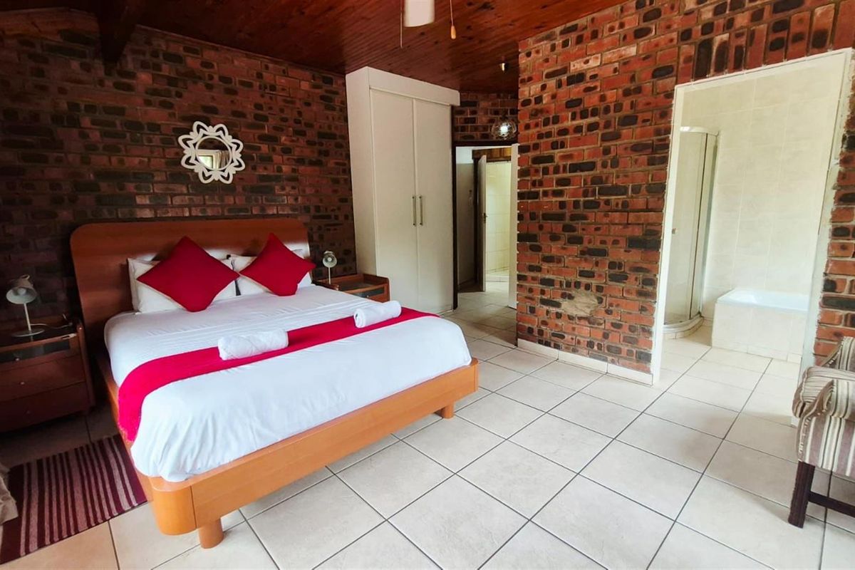 Spacious bedroom featuring exposed brick walls, timber ceiling, built-in wardrobe, and an en-suite bathroom with a shower and bathtub.