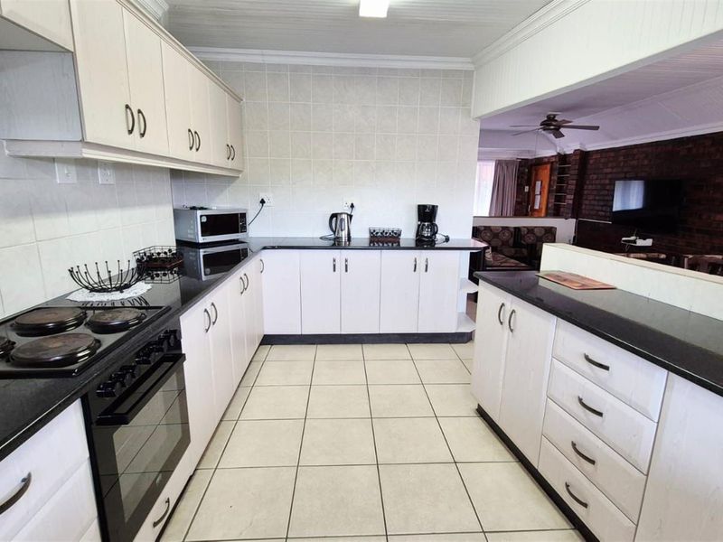 Open-plan kitchen featuring white cabinetry, black granite countertops, tiled flooring, and a breakfast bar overlooking the adjacent living area.