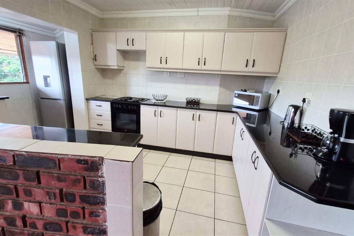 A functional kitchen featuring built-in cabinetry, granite countertops, a built-in oven and hob, and a breakfast bar with a brick feature wall.