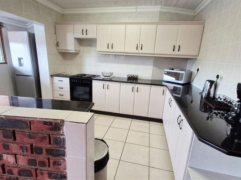 A functional kitchen featuring built-in cabinetry, granite countertops, a built-in oven and hob, and a breakfast bar with a brick feature wall.