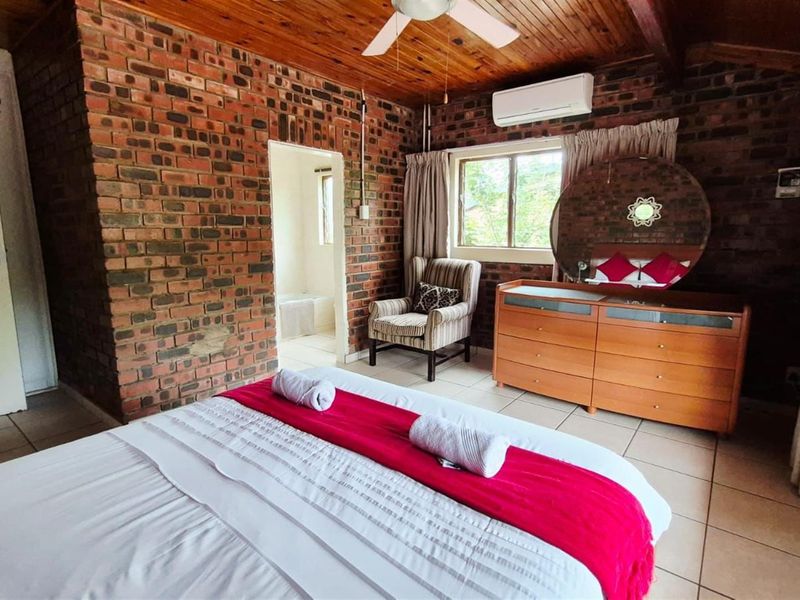 A bedroom featuring exposed brick walls, a timber-clad ceiling with a fan, tiled flooring, and an integrated air conditioning unit.