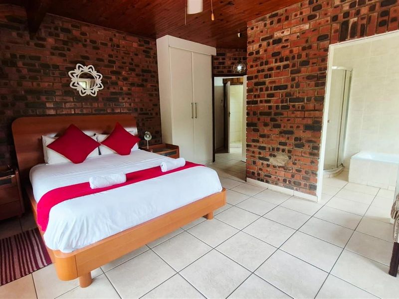 Spacious bedroom featuring exposed brick walls, timber ceiling, tiled flooring, built-in wardrobe, and direct access to an en-suite bathroom.
