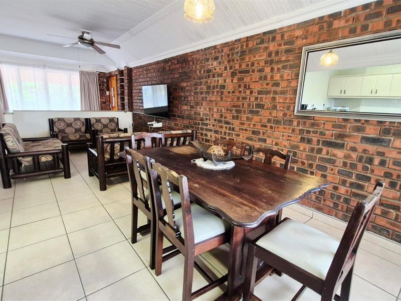 Spacious open-plan living and dining area featuring a distinctive exposed brick wall, tiled flooring, and a vaulted beadboard ceiling with a fan.