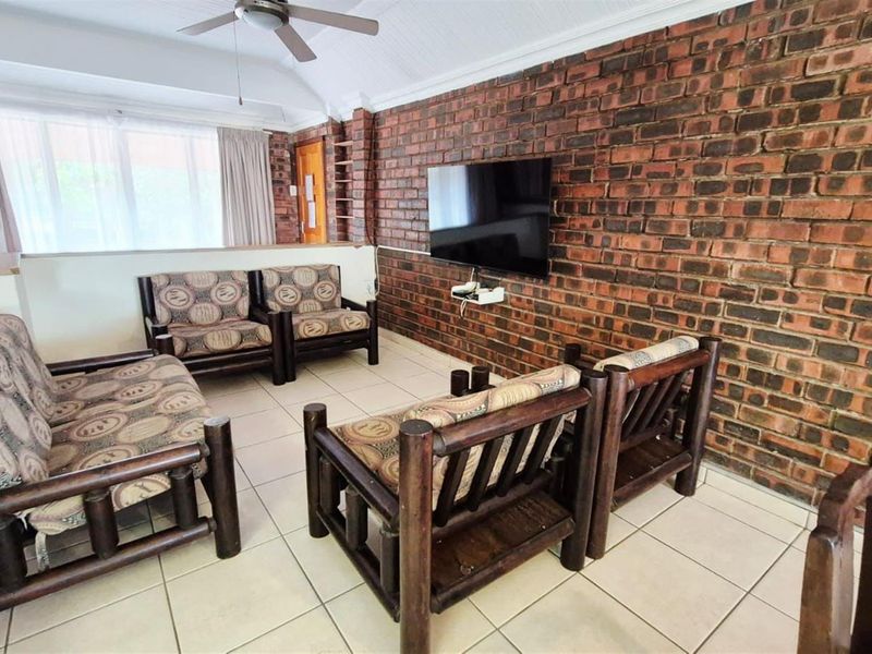 A living room featuring a prominent exposed brick feature wall, vaulted ceilings with a fan, and neutral tiled flooring.