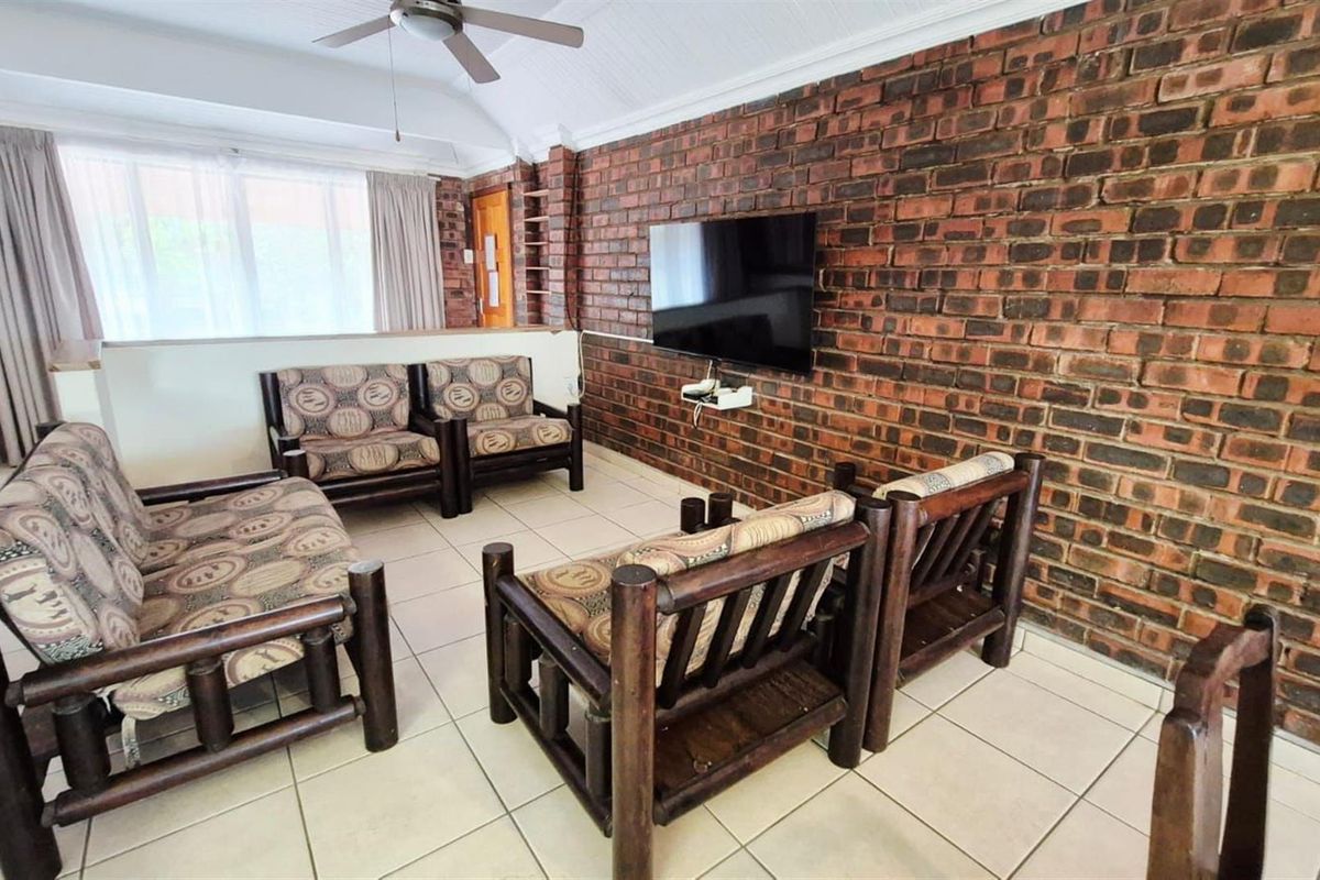 A living room featuring a prominent exposed brick feature wall, vaulted ceilings with a fan, and neutral tiled flooring.