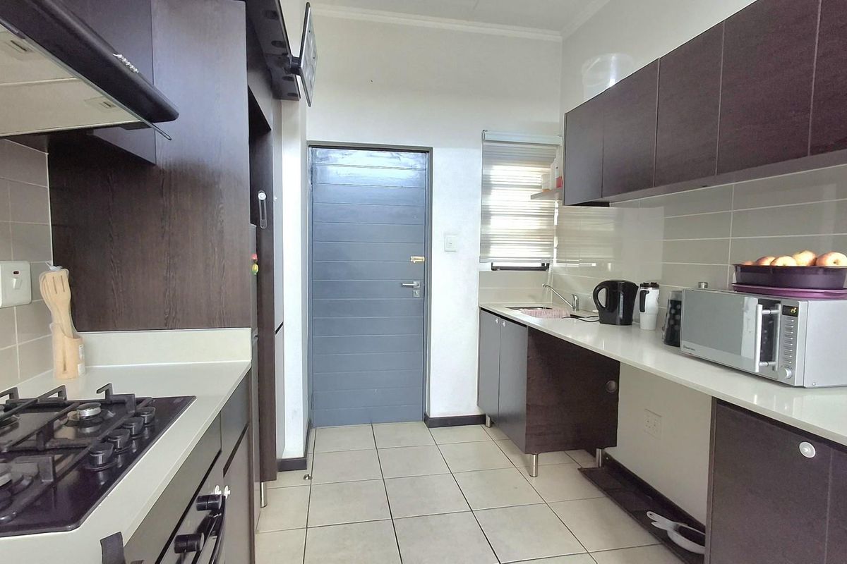 A functional kitchen featuring dark wood cabinetry, light-colored countertops, a built-in gas hob, extractor fan, and tiled flooring.