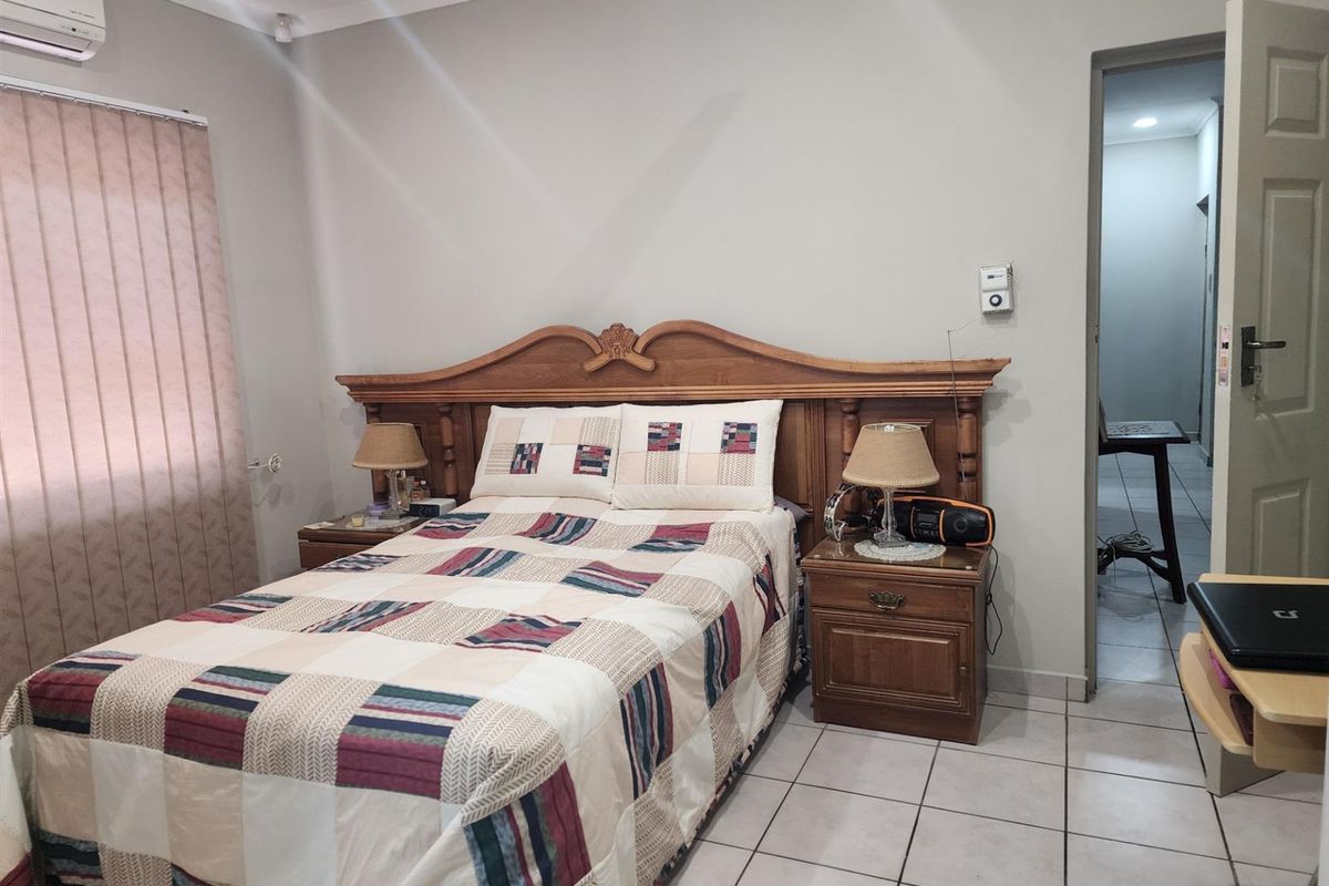 A bedroom featuring tiled flooring, a wall-mounted air conditioning unit, and vertical blinds.