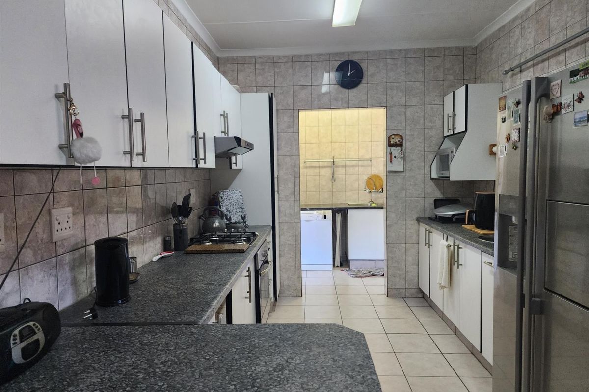 A functional kitchen featuring white cabinetry, granite-look countertops, and tiled walls, with an adjoining scullery area visible through the doorway.