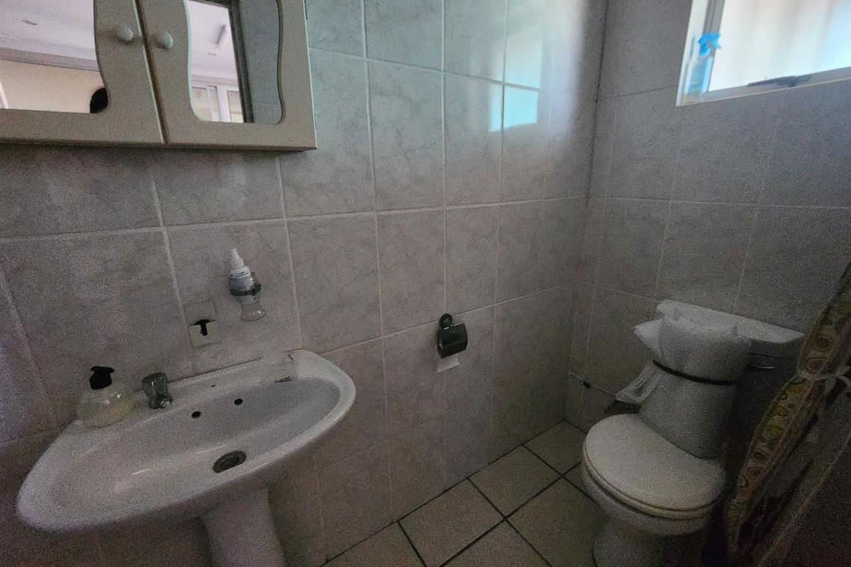 A functional guest bathroom featuring a pedestal basin, wall-mounted medicine cabinet, and a standard toilet with full-height wall tiling.
