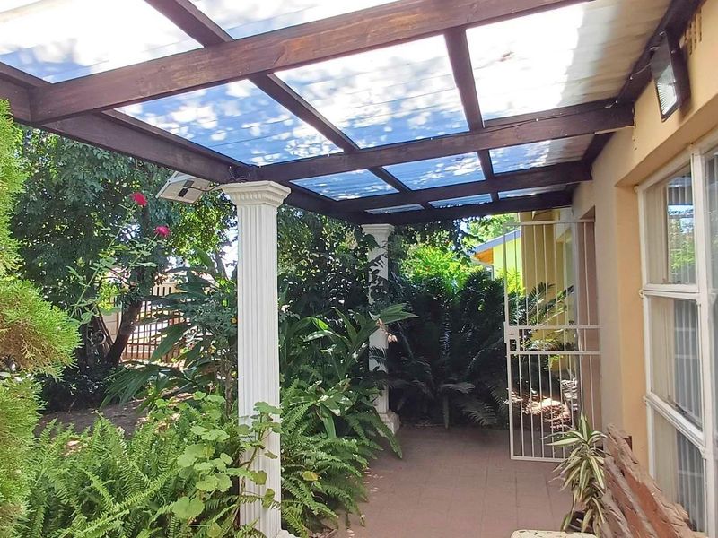 A covered patio area featuring a timber pergola with polycarbonate roofing, decorative columns, and direct access to the garden.