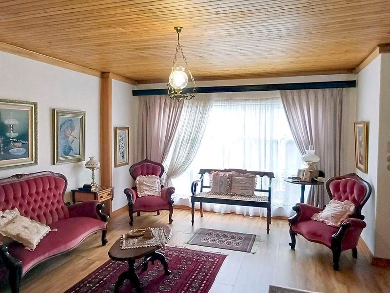 A traditional living room featuring a warm timber-clad ceiling, laminate flooring, and direct access to an outdoor area through a security gate.