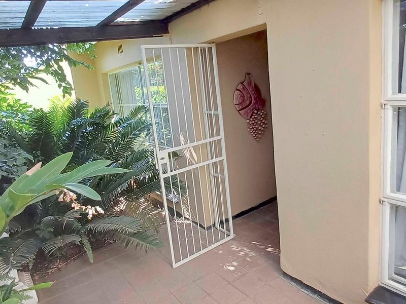 A covered patio area featuring tiled flooring, a security gate, and a pergola structure, providing a sheltered outdoor space.