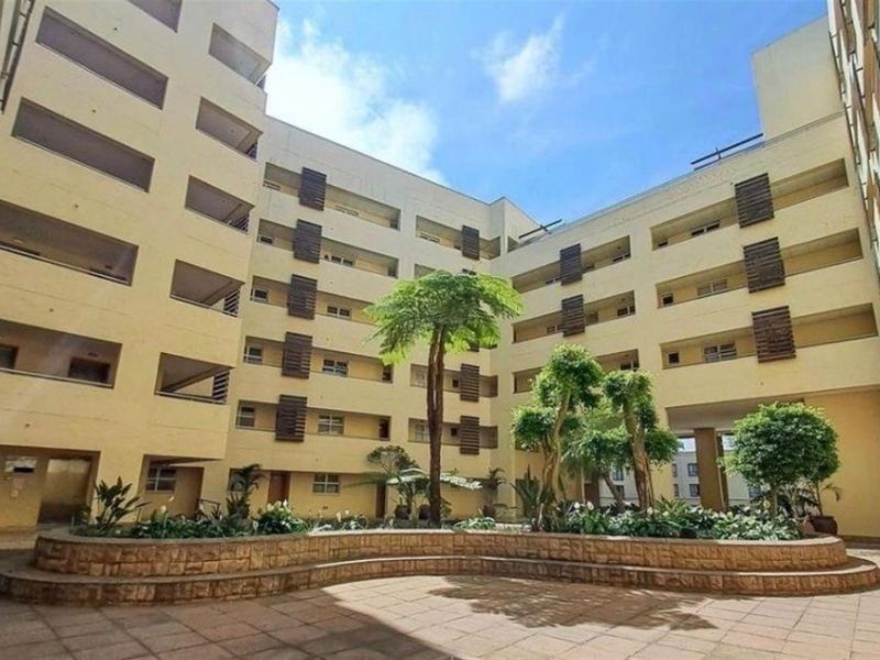 A central courtyard area within an apartment complex, featuring paved ground, landscaped garden beds, and multi-story residential building facades.