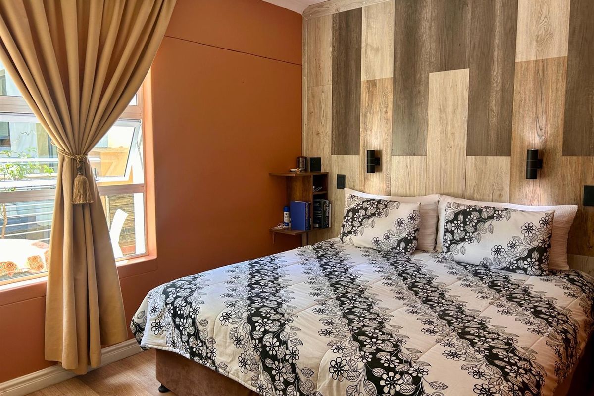 A bedroom featuring a wood-look accent wall, wall-mounted bedside lighting, and a window with curtain treatments.