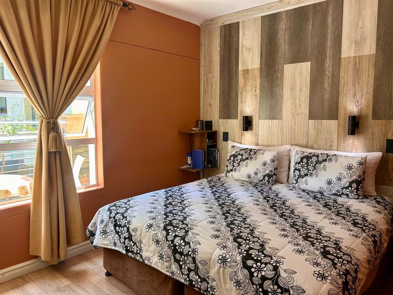 A bedroom featuring a wood-look accent wall, wall-mounted bedside lighting, and a window with curtain treatments.