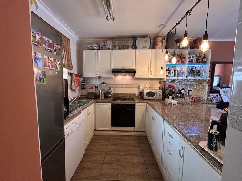 A functional kitchen featuring white cabinetry, granite countertops, a built-in oven, hob, extractor fan, and a breakfast bar with pendant lighting.