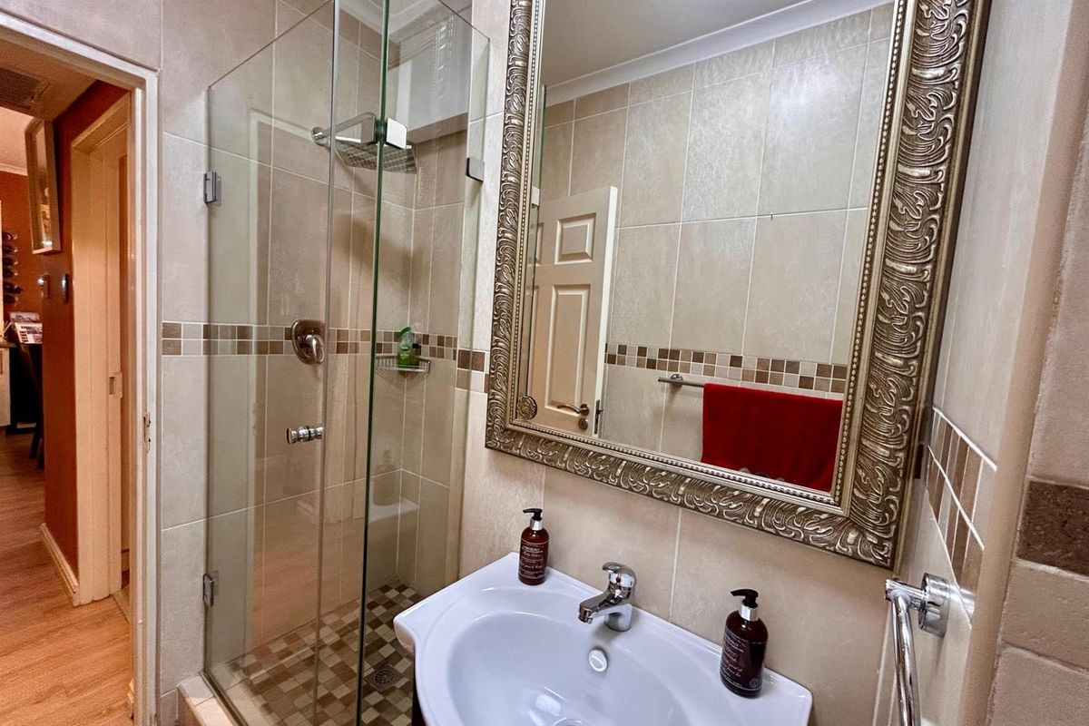 A compact bathroom featuring a glass-enclosed shower, a pedestal basin, and neutral wall tiling with a decorative mosaic border.