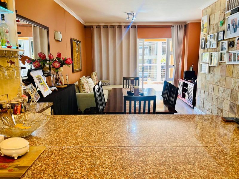 Open-plan living and dining area featuring a granite-topped breakfast counter, stone-clad feature wall, and sliding door access to a private balcony.