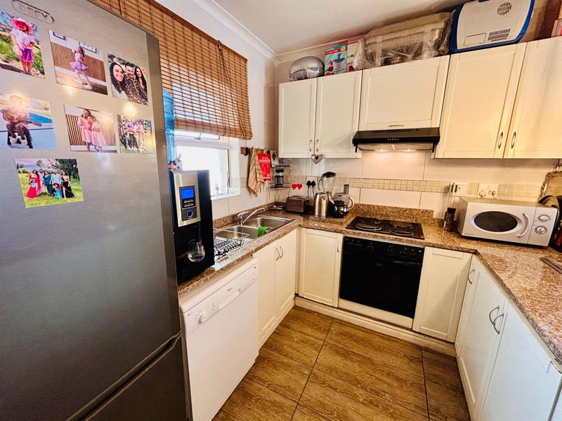 Compact kitchen featuring white cabinetry, granite countertops, tiled backsplash, built-in oven, hob, and extractor fan with tiled flooring.