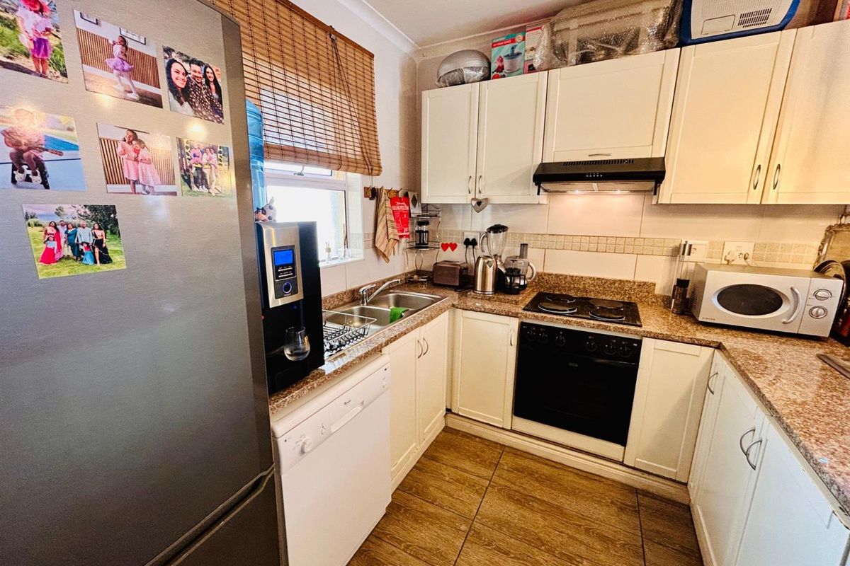 Compact kitchen featuring white cabinetry, granite countertops, tiled backsplash, built-in oven, hob, and extractor fan with tiled flooring.