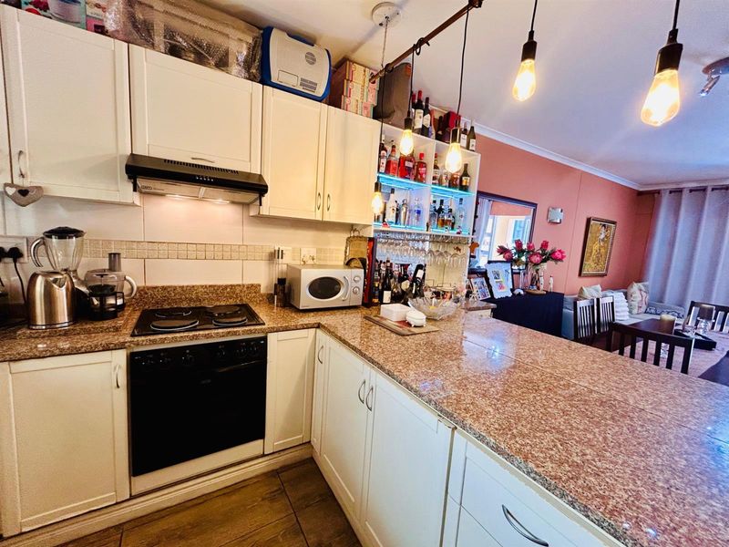 Open plan kitchen featuring granite countertops, built-in cabinetry, an integrated oven and hob, and a breakfast bar overlooking the living area.