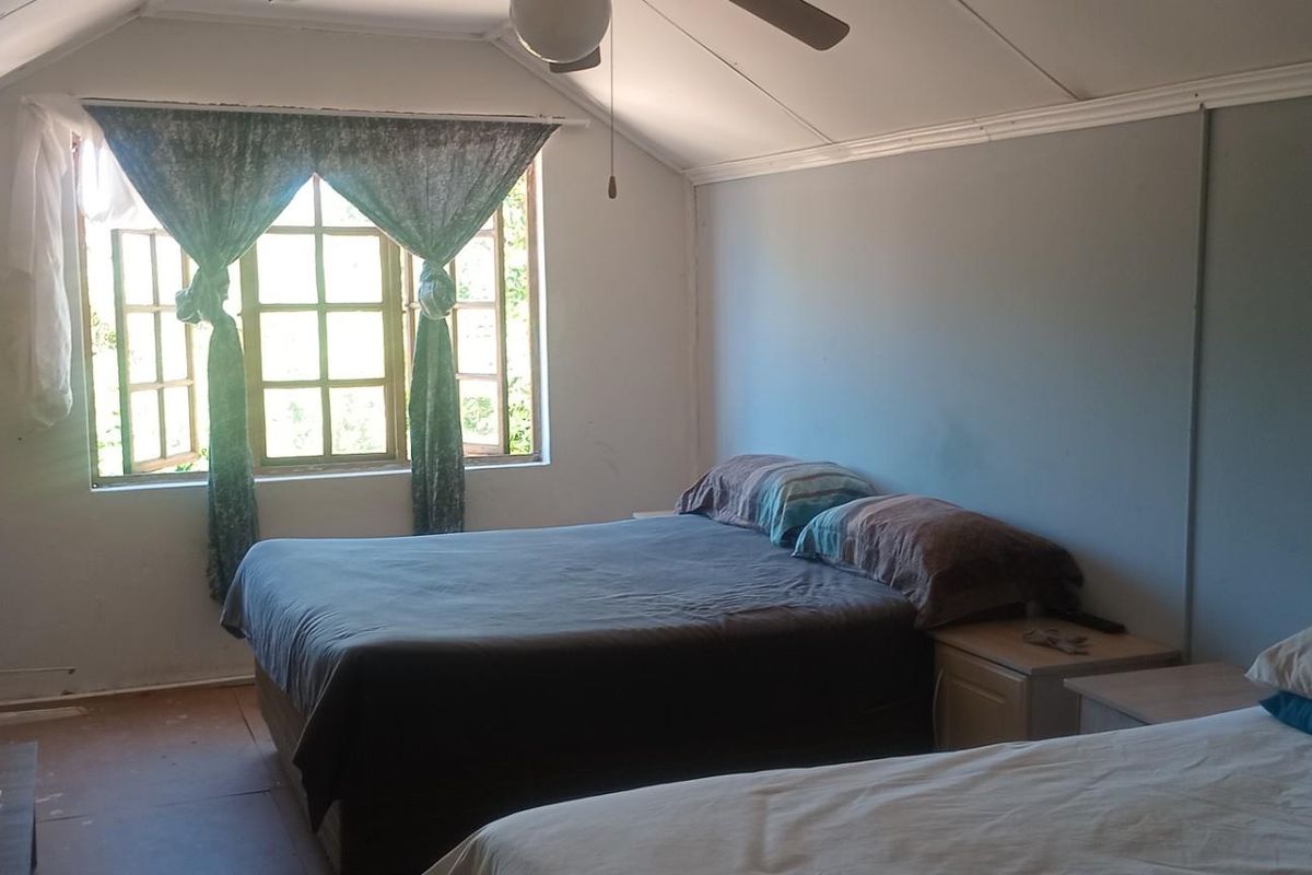 A bedroom featuring a pitched ceiling, timber-framed windows, and a ceiling fan, offering a functional space with potential for cosmetic updates.