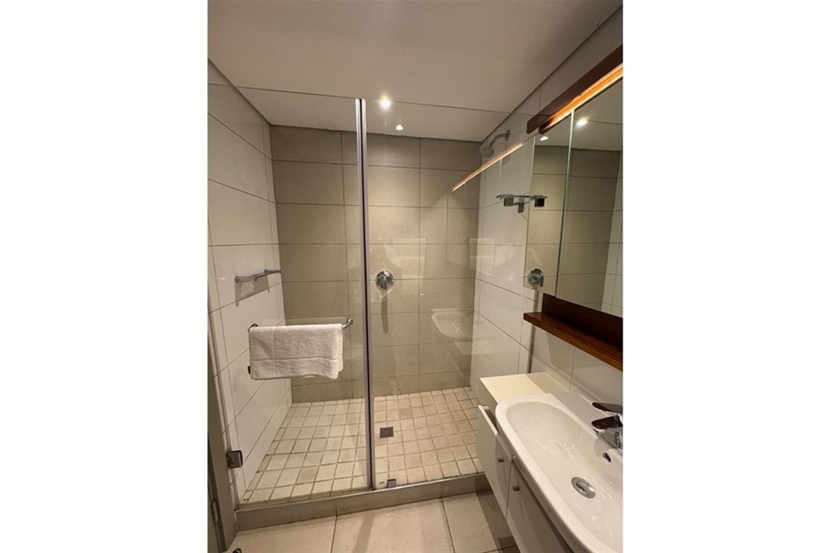 A modern bathroom featuring a glass-enclosed shower, a wall-mounted vanity with a basin, and neutral wall and floor tiling.