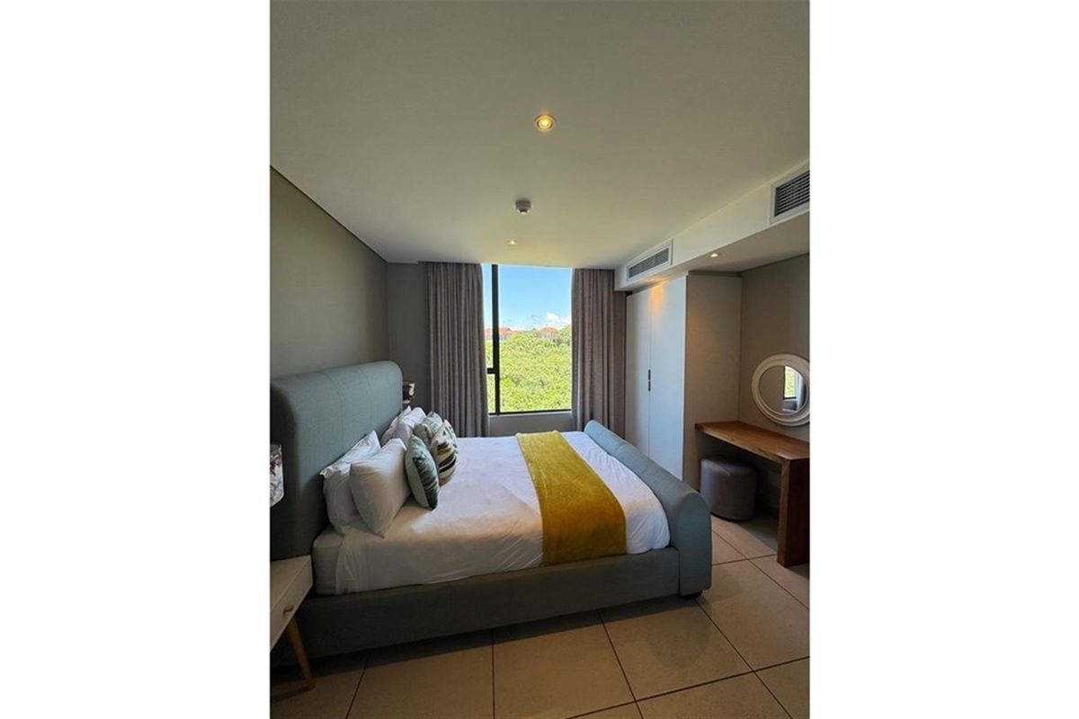 A well-maintained bedroom featuring tiled flooring, built-in cabinetry, recessed ceiling lighting, and a large window with views of the surrounding greenery.