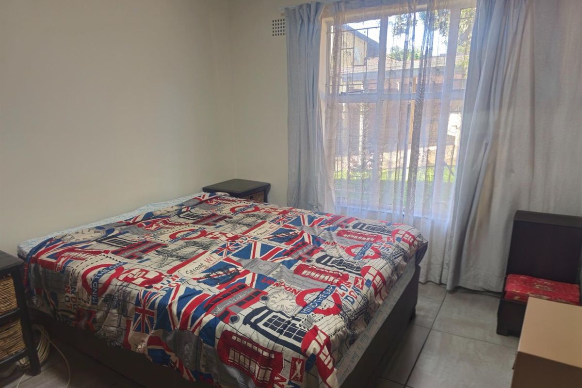 A functional bedroom featuring tiled flooring and a large window with security bars, providing natural light.