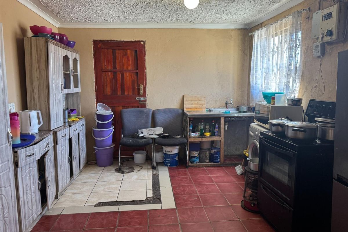 A dated kitchen area featuring tiled flooring, basic cabinetry, and a freestanding stove, requiring significant renovation and modernization of finishes.