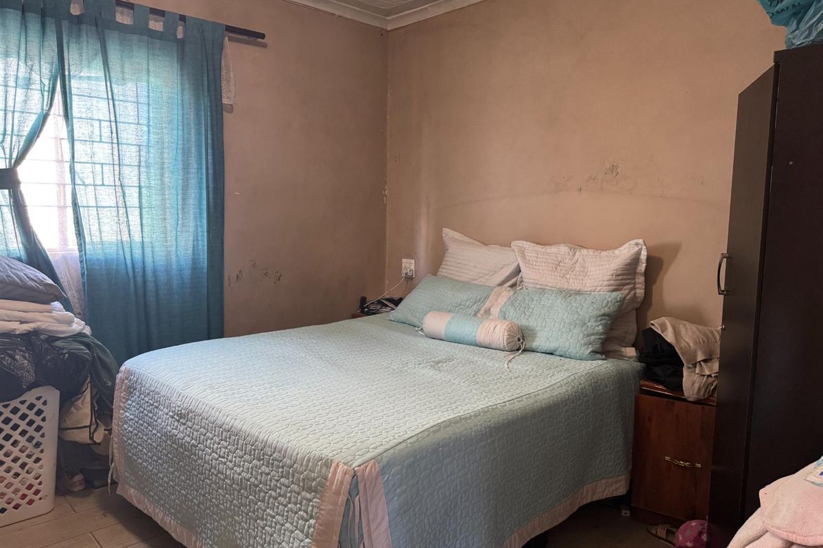 A bedroom featuring tiled flooring, a window with security bars, and a textured ceiling finish, requiring cosmetic updates to the wall surfaces.